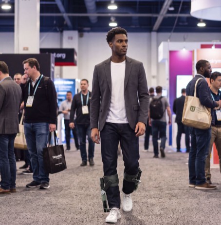 A man wearing Sidekick robots walking through a busy expo hall